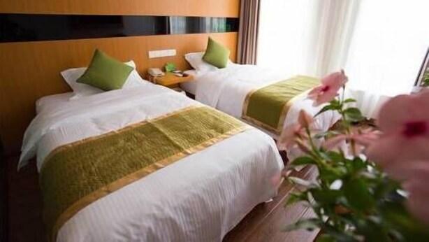 Dos camas con ropa de cama verde y blanca, un cabecero de madera y una mesita de noche con una lámpara.