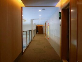 A hotel corridor with a carpeted floor, glass railings, and a digital elevator display.