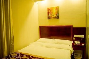 A hotel room with a bed, a painting on the wall, and a nightstand with a phone.