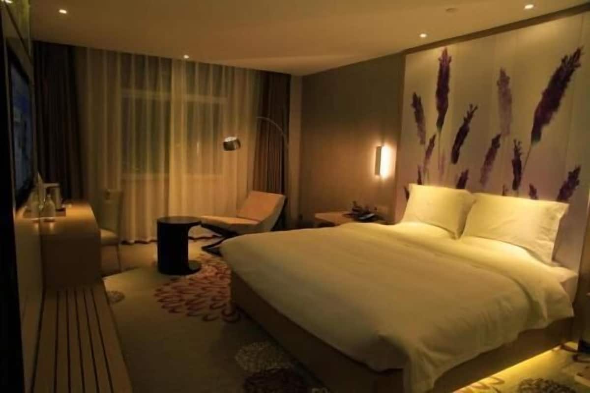 Hotellihuone, jossa on sänky, tuoli, pieni pöytä ja koristeellinen seinä.