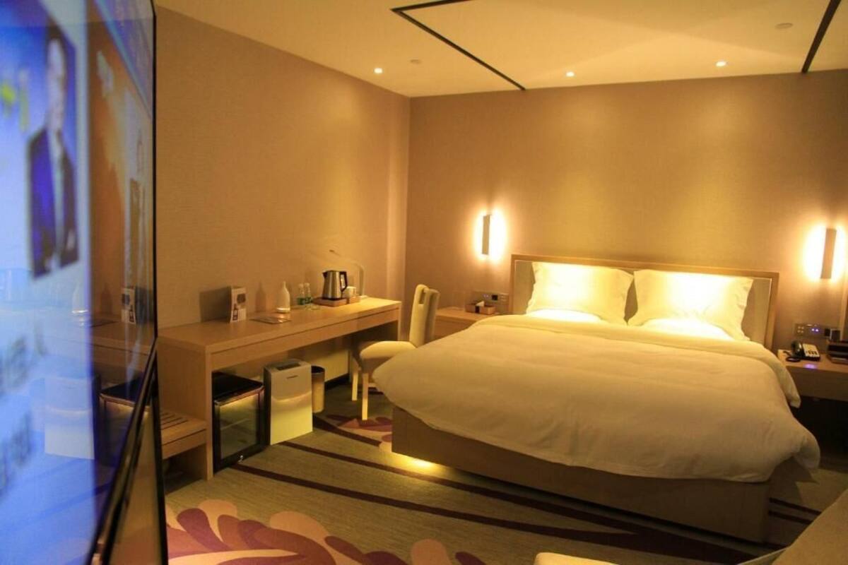 Hotellihuone, jossa on suuri sänky, työpöytä tuolilla, pieni pöytä ja televisio.