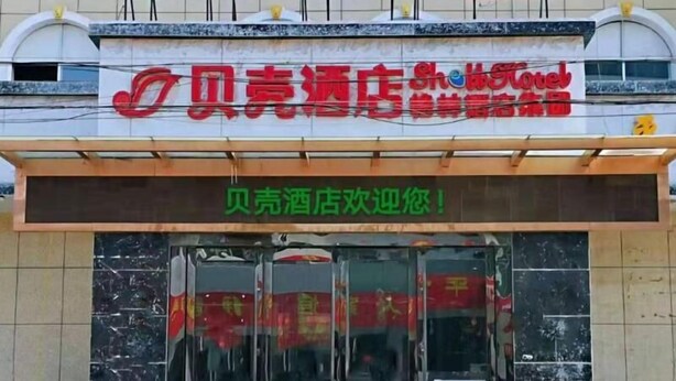 A hotel entrance with a glass door, a red sign above, and a welcome message in green. - Shell Hotel (Yangzhou)