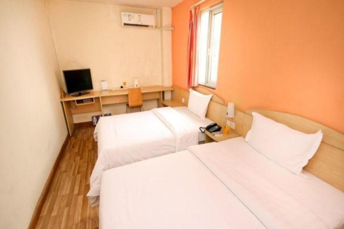A hotel room with two beds, a desk with a computer, a TV, and a window with curtains.