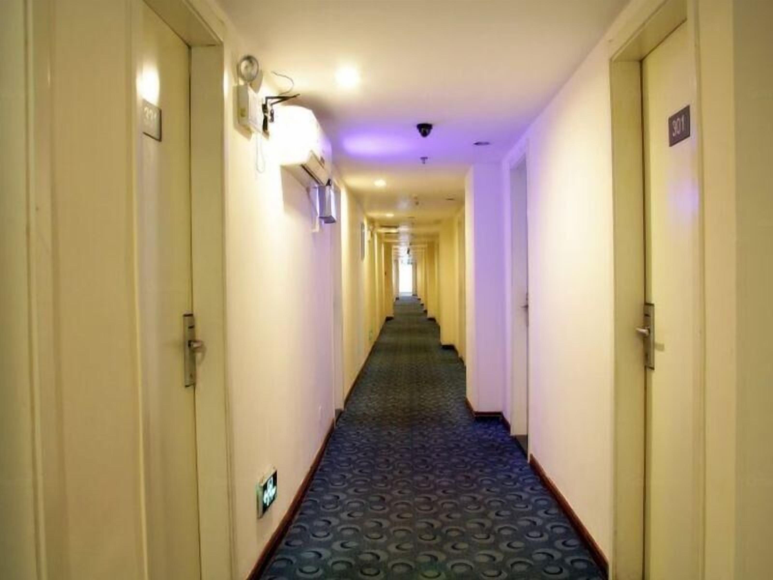 Corredor de hotel com portas em ambos os lados, um carpete estampado e um candeeiro na parede.