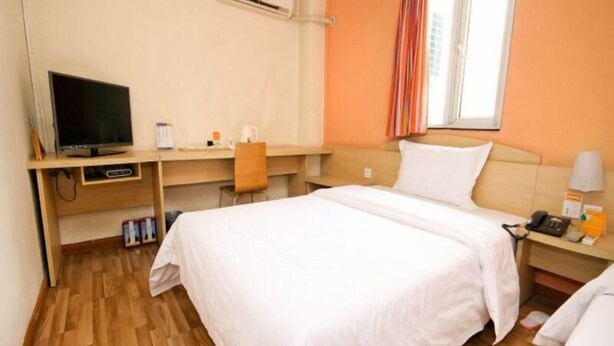 Quarto de hotel com cama, escrivaninha, televisão e ar condicionado.