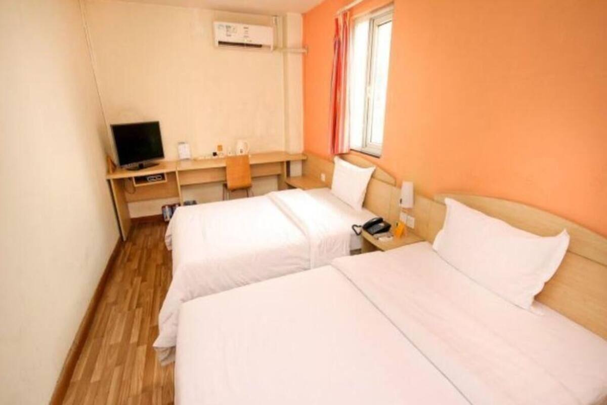Habitación de hotel con dos camas, un escritorio con computadora, televisión y ventana con cortinas.