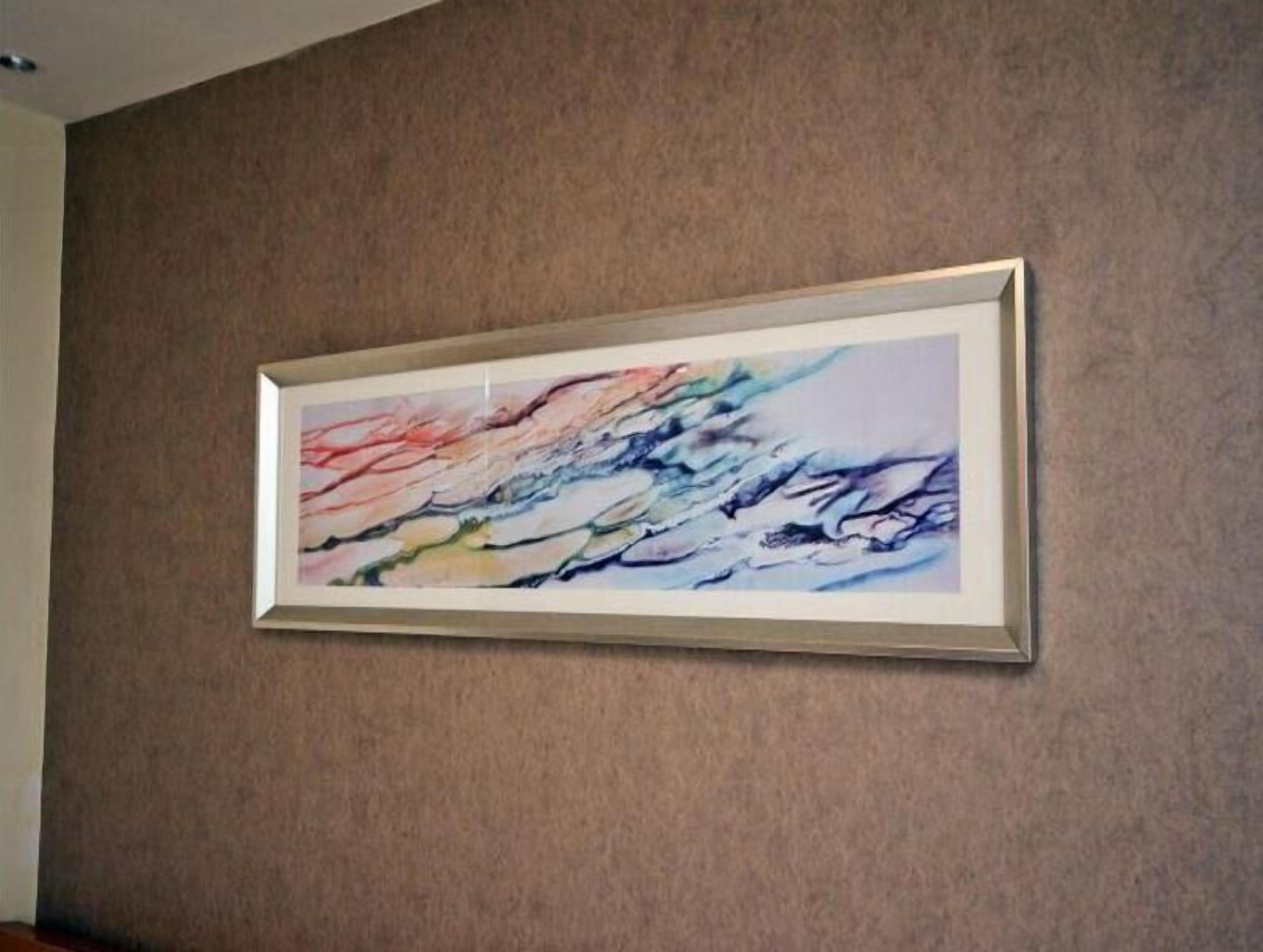 A framed abstract painting on a textured wall.