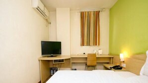 Quarto de hotel com cama, secretária com televisão, cadeira e janela com cortinas listradas.
