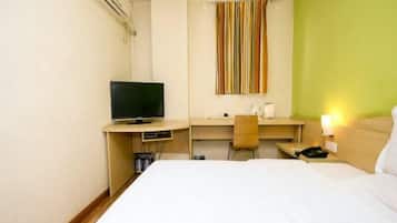 Quarto de hotel com cama, secretária com televisão, cadeira e janela com cortinas listradas.