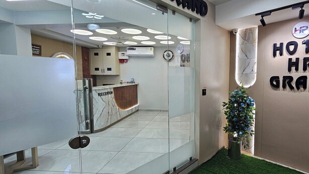 Un espace d’accueil comprenant un comptoir, un bureau de réception, un climatiseur fixé au mur et une enseigne indiquant « HÔTEL HR GRAND ».