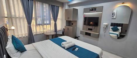 Ein Hotelzimmer mit einem Bett, einem Schreibtisch, einem Fernseher, einem Spiegel und einem Schild mit dem Hotelnamen.