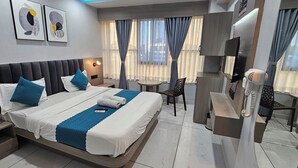Une chambre d’hôtel comprenant un lit, des tables de chevet, un bureau, une chaise, une télévision et des rideaux.