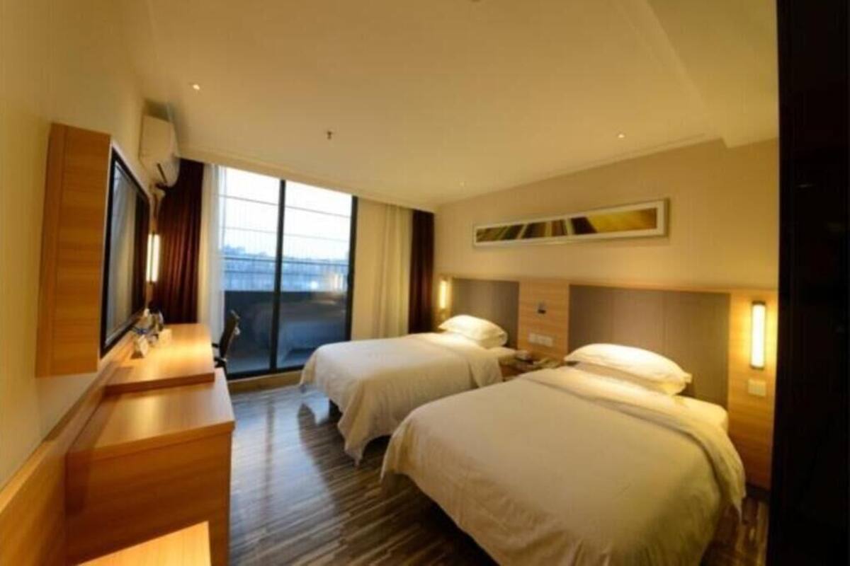 Habitación de hotel con dos camas, un escritorio, un televisor y un ventanal grande.