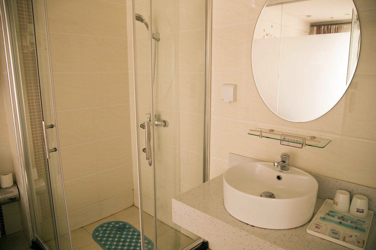 Un baño con cabina de ducha de vidrio, lavamanos con espejo y artículos de aseo en la encimera.