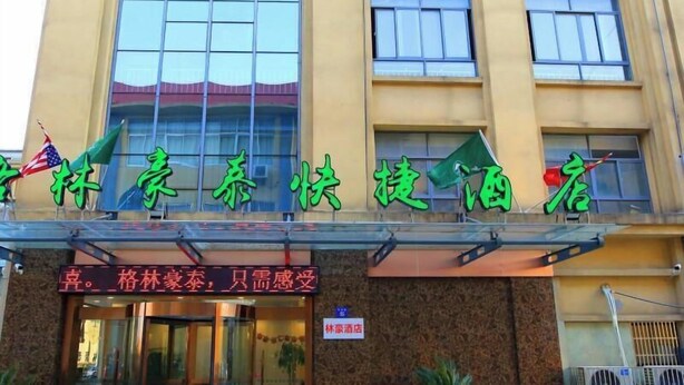 A hotel facade with a sign in Chinese characters, an American flag, and a neon sign indicating a restaurant. - Greentree Express Hotel (Wuxi)
