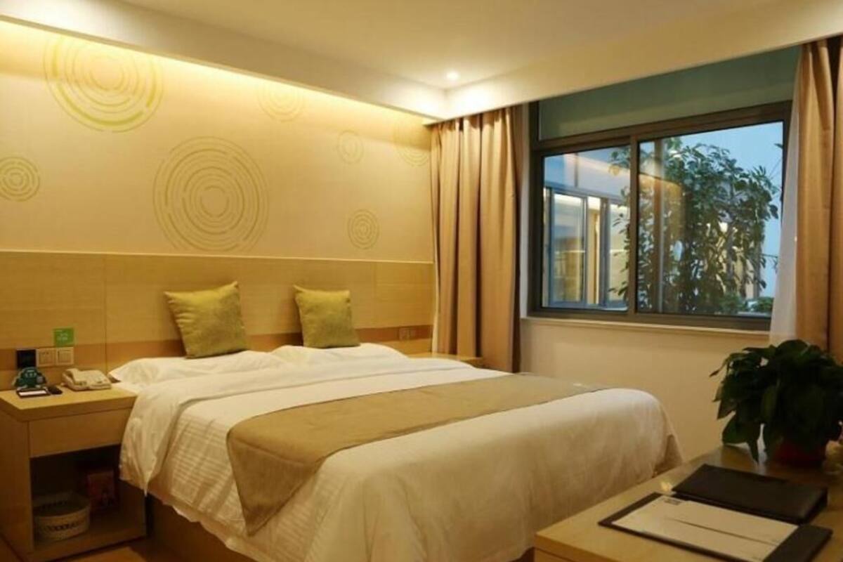 A hotel room with a bed, bedside table, and a window with curtains.
