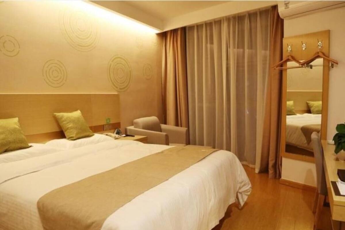A hotel room with a large bed, a desk, a chair, and a mirror.