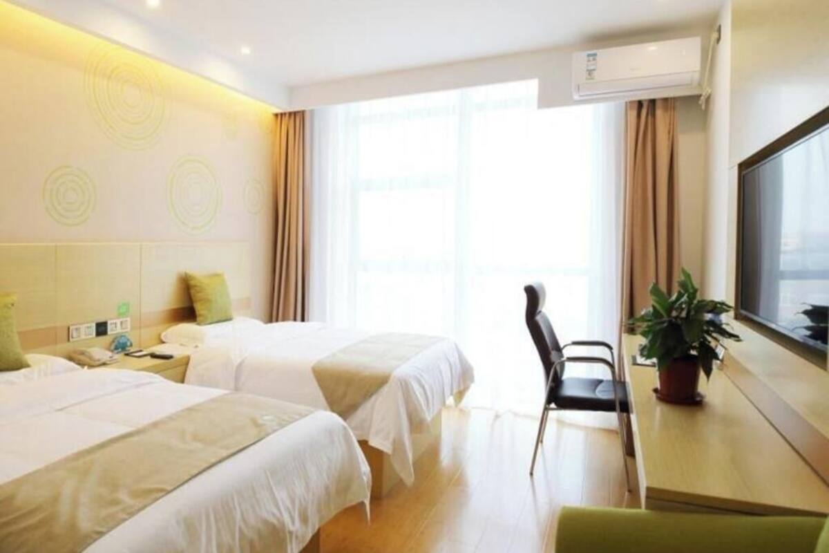 A hotel room with two beds, a desk with a chair, a potted plant, and a large window.