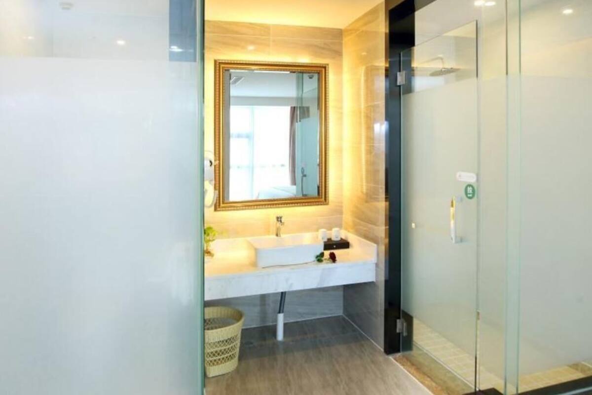 A modern bathroom with a glass shower enclosure, a white sink with a gold-framed mirror, and a small wicker basket.