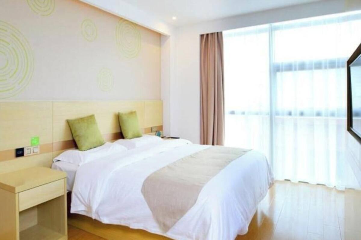 A hotel room with a large bed, a bedside table, a headboard with circular patterns, and a large window with curtains.