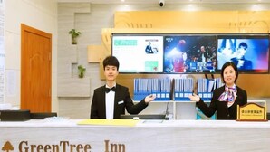 A reception desk at GreenTree Inn with a digital display, a wooden door, and a plant. - Greentree Express Hotel (Wuxi)