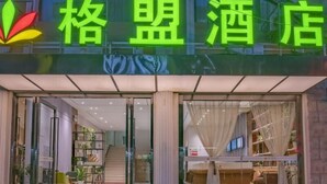 A hotel entrance with a green neon sign, glass doors, and a visible interior with a staircase and seating area.