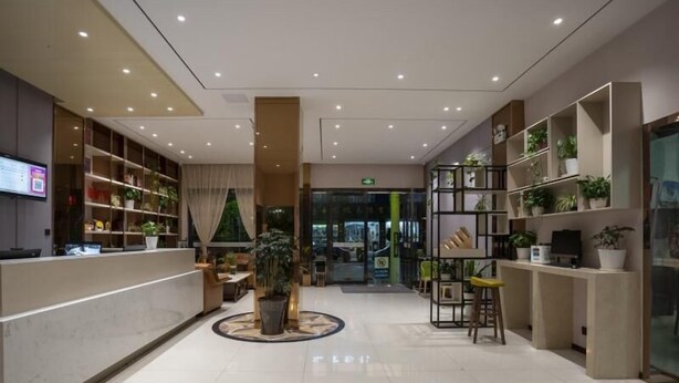 A modern hotel lobby with a reception desk, seating area, and potted plants.