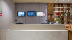 A reception desk with three monitors, a bookshelf with books and plants, and a leather couch.