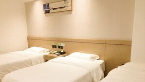 A hotel room with two beds, a wooden headboard, a bedside table with a lamp, a phone, and a small clock.