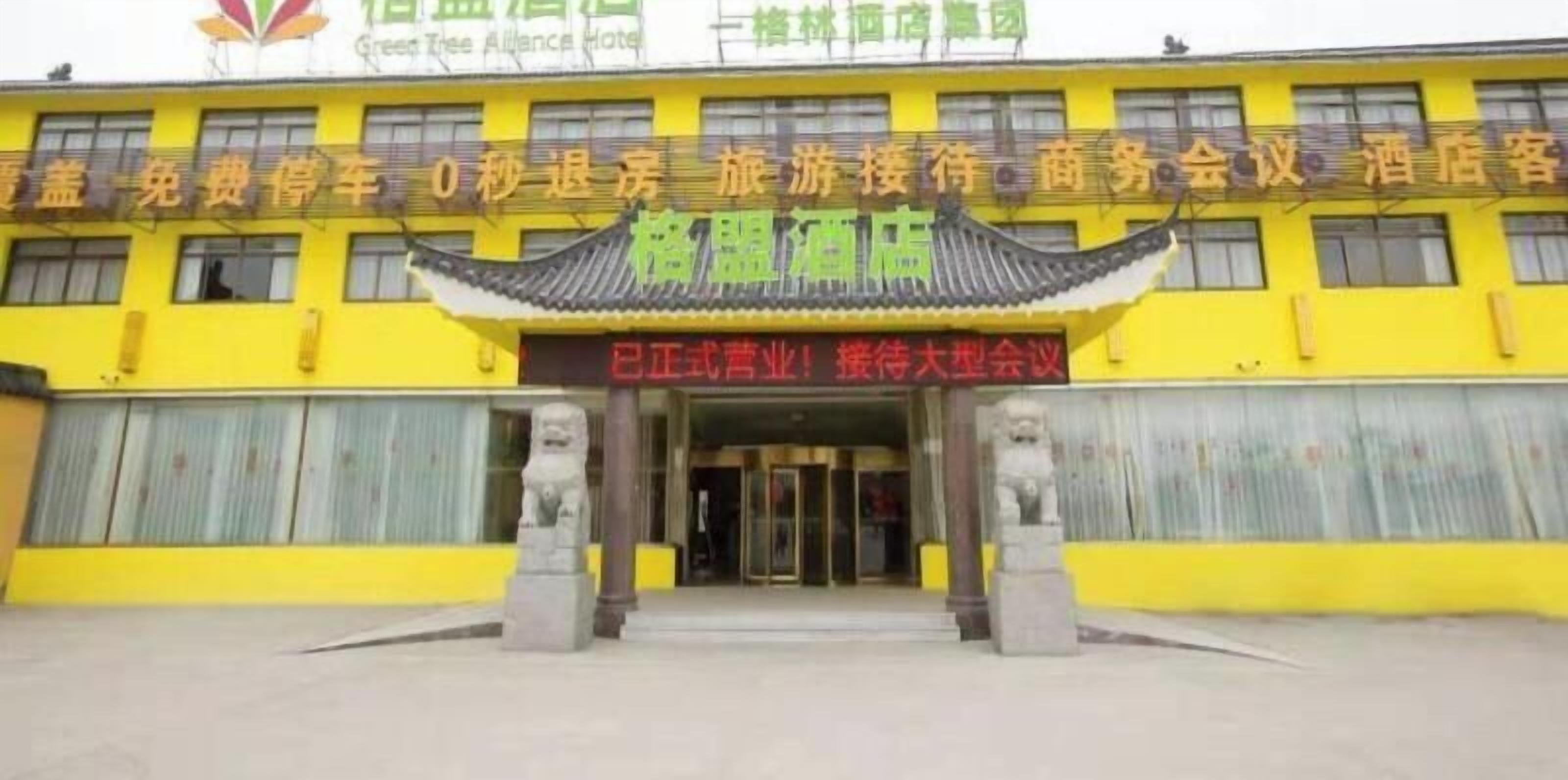 Um hotel com fachada amarela, elementos arquitetônicos chineses tradicionais e uma placa indicando que pertence ao grupo Green Tree Alliance Hotel.