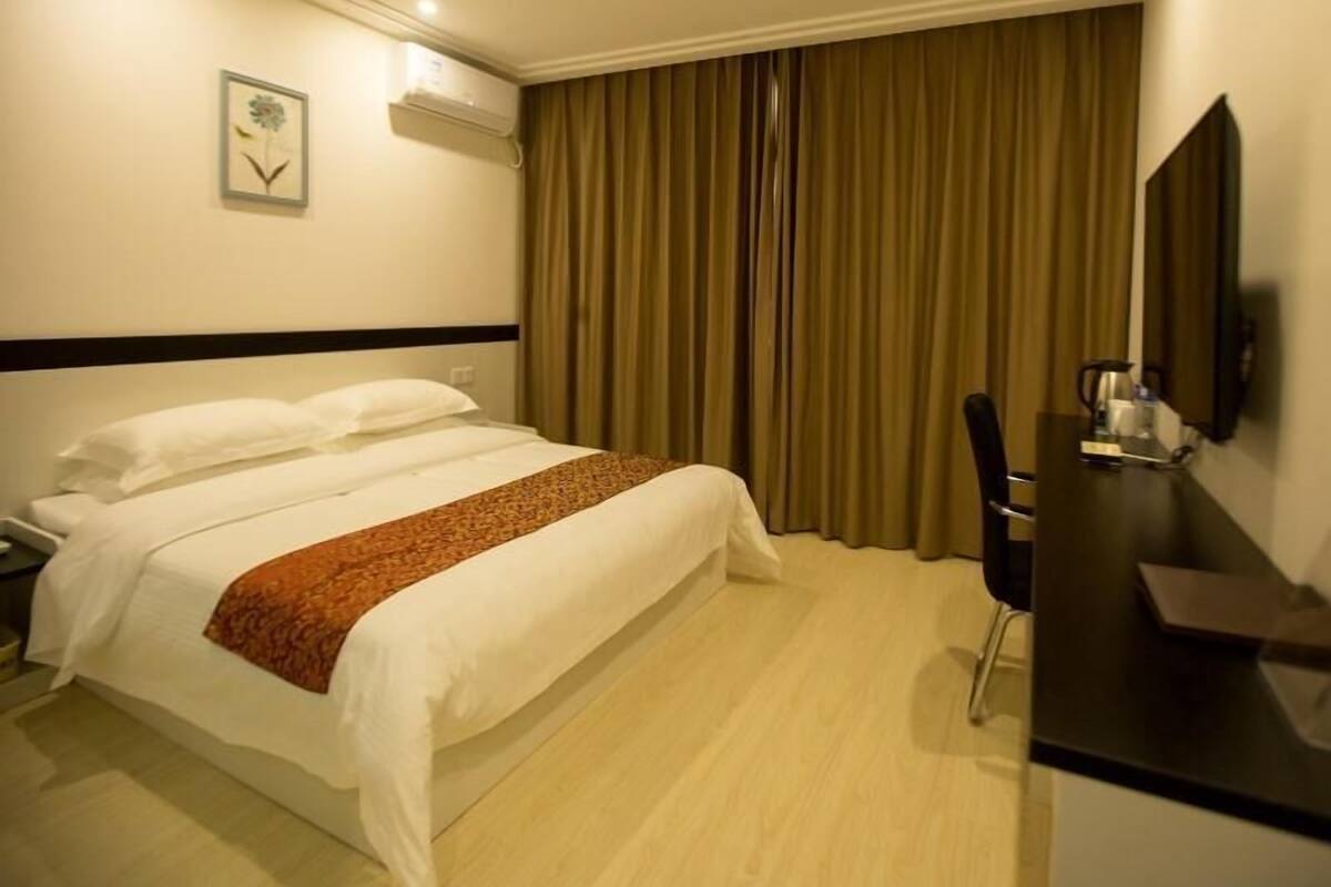 Ein Hotelzimmer mit Bett, Schreibtisch, Stuhl, Fernseher und einem fensterbepflanzten Fenster.