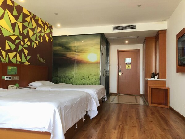 A hotel room with two beds, a large wall mural, a wooden door, and a small bathroom area.