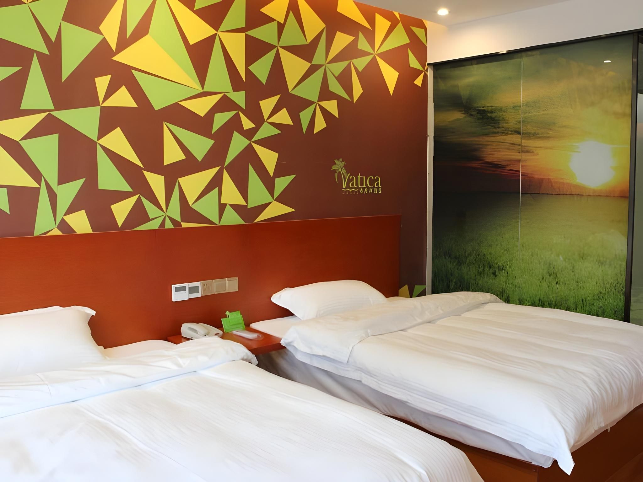 Habitación de hotel con dos camas, una pared con motivos geométricos y un ventanal con vistas a un atardecer.