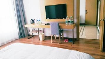 A hotel room with a large bed, a desk with a television, and a chair.