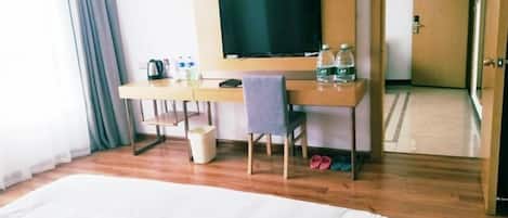 A hotel room with a large bed, a desk with a television, and a chair.