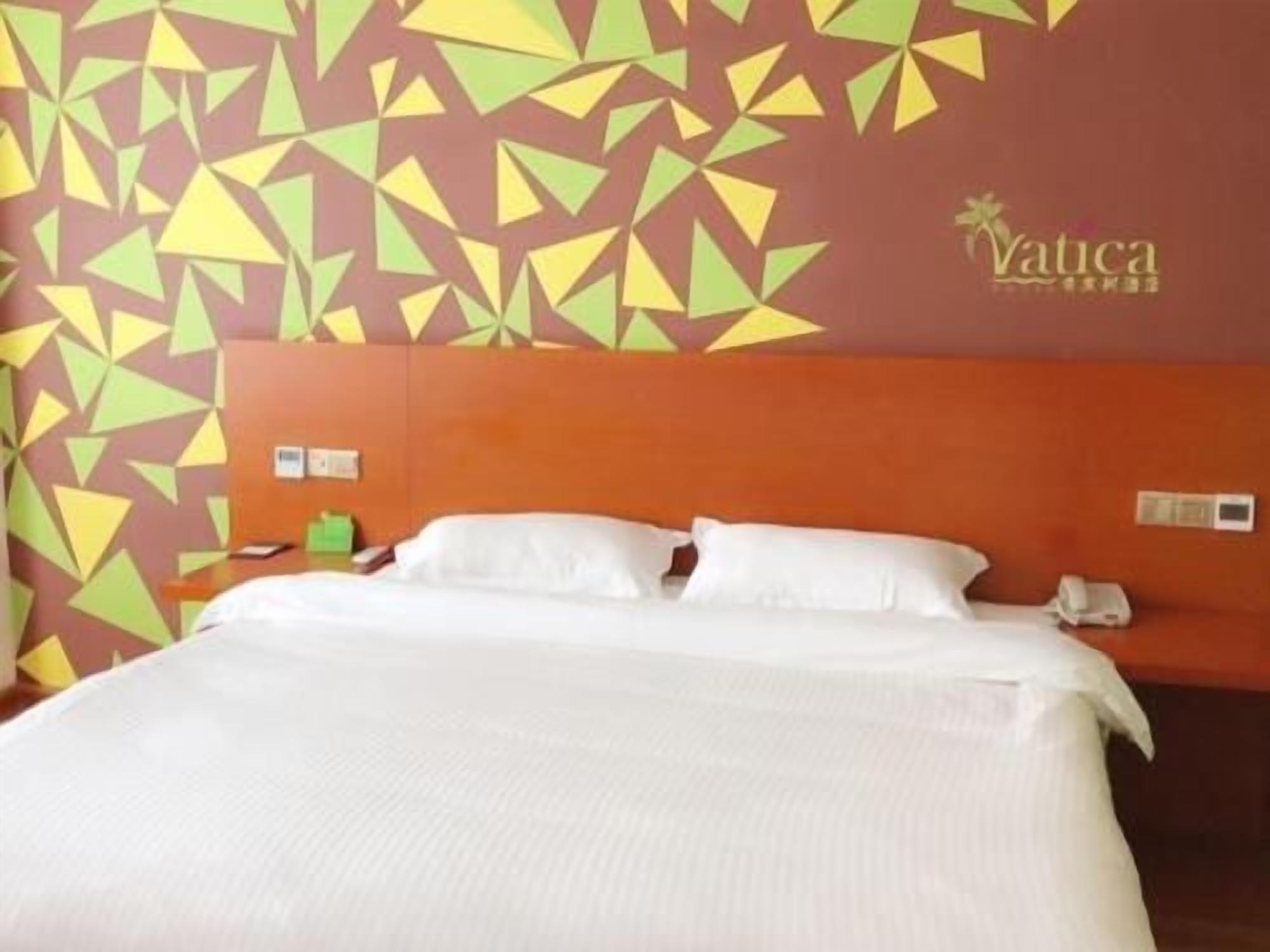 Quarto de hotel com cama, cabeceira, parede com padrões geométricos e um logotipo.