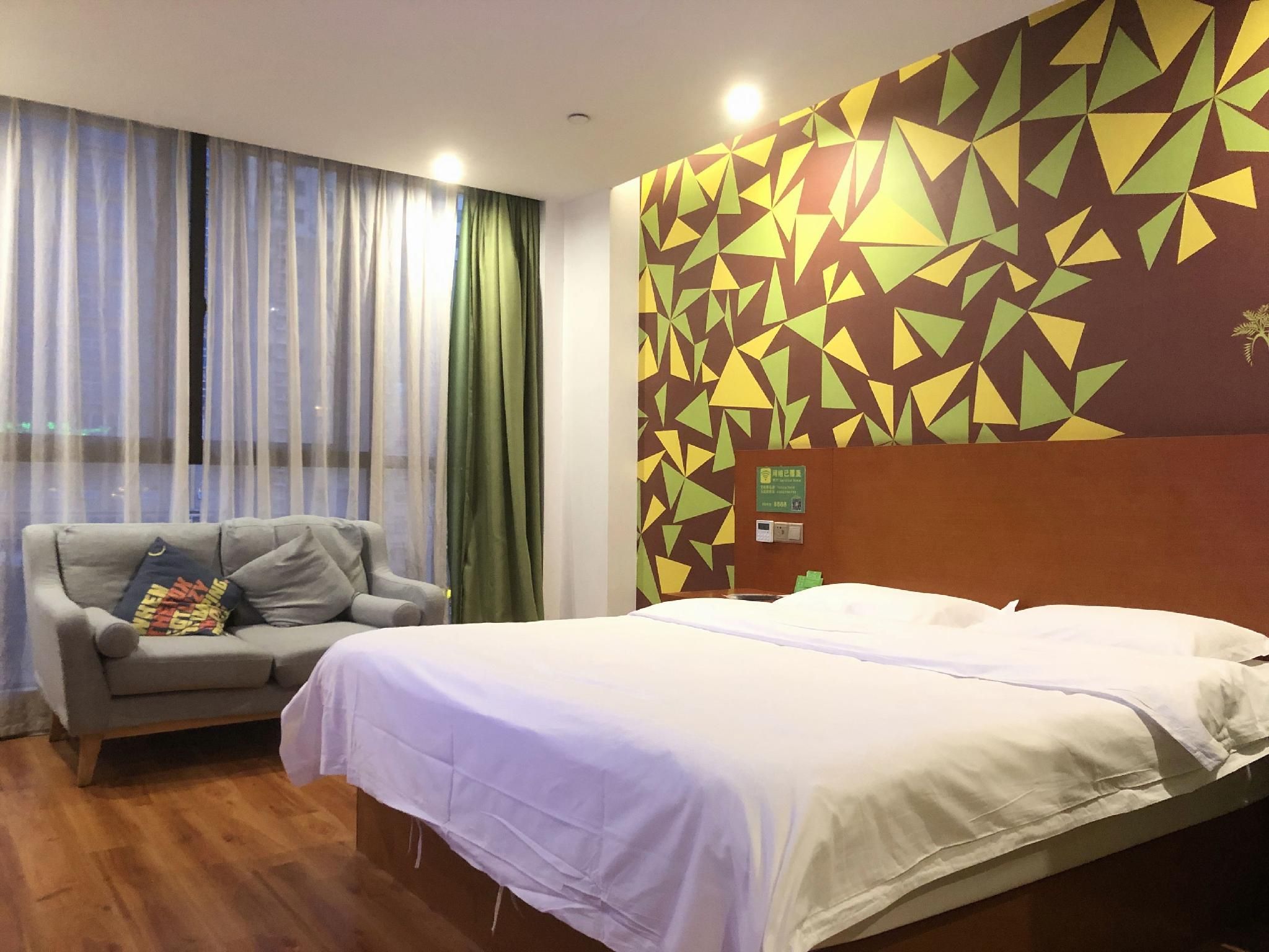 A hotel room with a bed, a sofa, a window with curtains, and a wall with a geometric pattern.