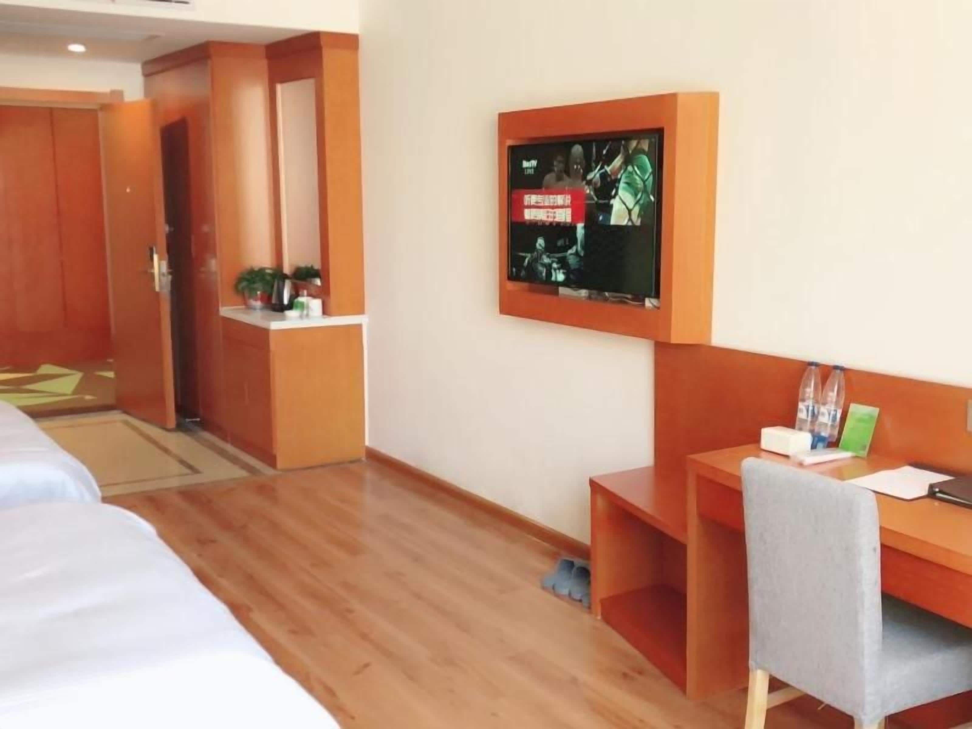 Une chambre d’hôtel comprenant un lit, un bureau, une chaise, un téléviseur fixé au mur et une armoire en bois.