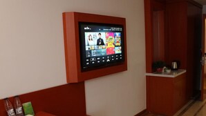 A hotel room with a mounted television displaying a movie, a wooden reception desk, and a small seating area. - Vatica Hotel Fuyang Linquan Tenghui International City Branch (Fuyang)