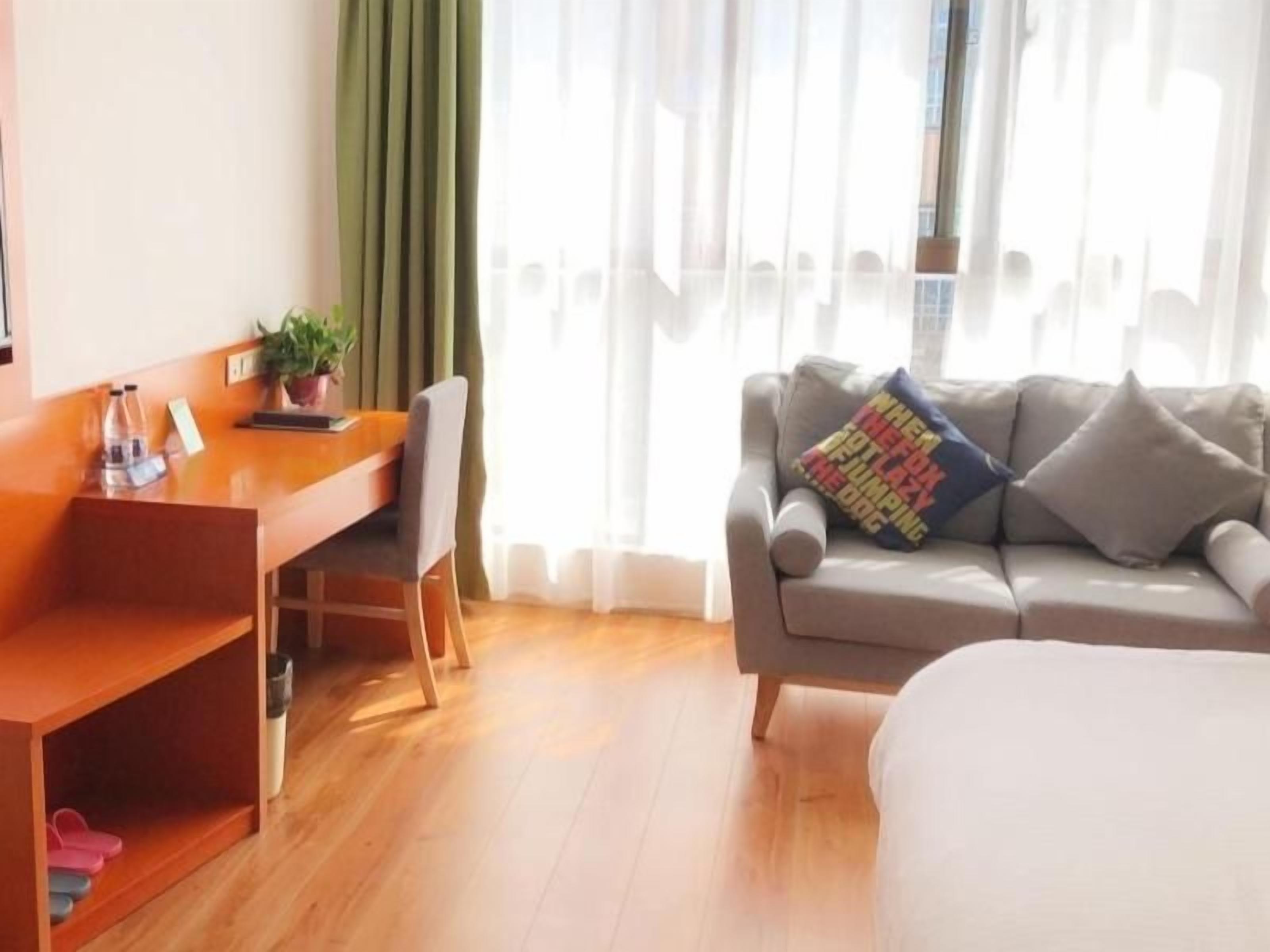 A hotel room with a wooden desk, a sofa, a bed, and a window with curtains.