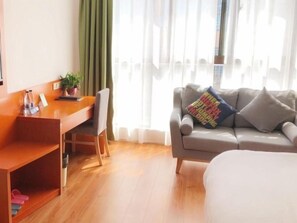 A hotel room with a wooden desk, a sofa, a bed, and a window with curtains.