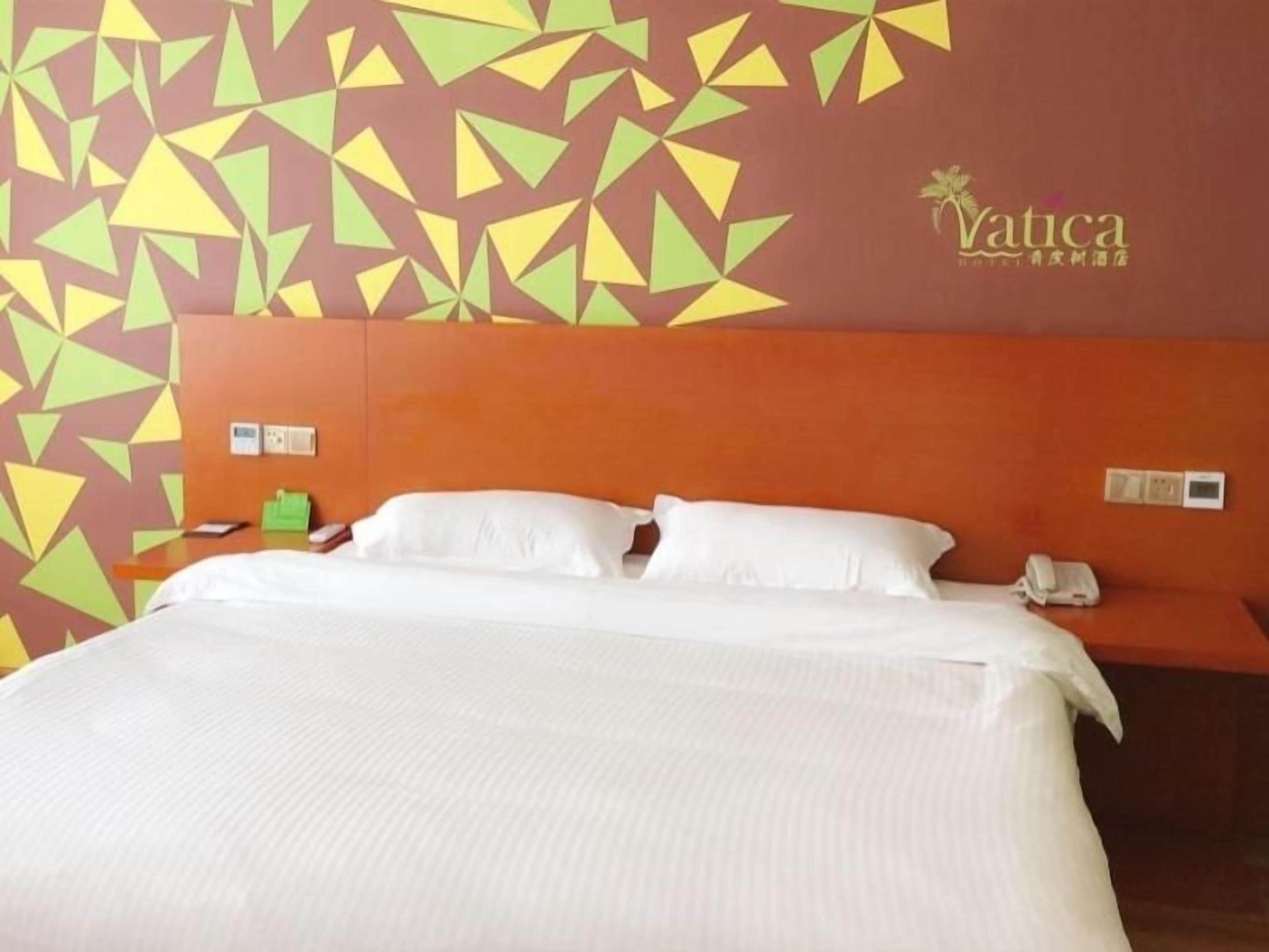 A hotel room with a bed, a headboard, a wall with geometric patterns, and a logo.
