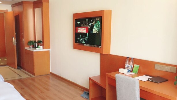 A hotel room with a wooden desk, a chair, a television mounted on the wall, and a bed in the background. - Vatica Hotel Fuyang Linquan Tenghui International City Branch (Fuyang)