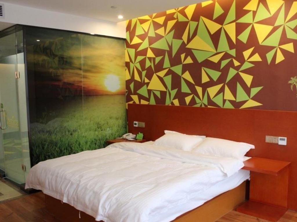 A hotel room with a bed, a nightstand, a glass partition, and a wall with geometric patterns.