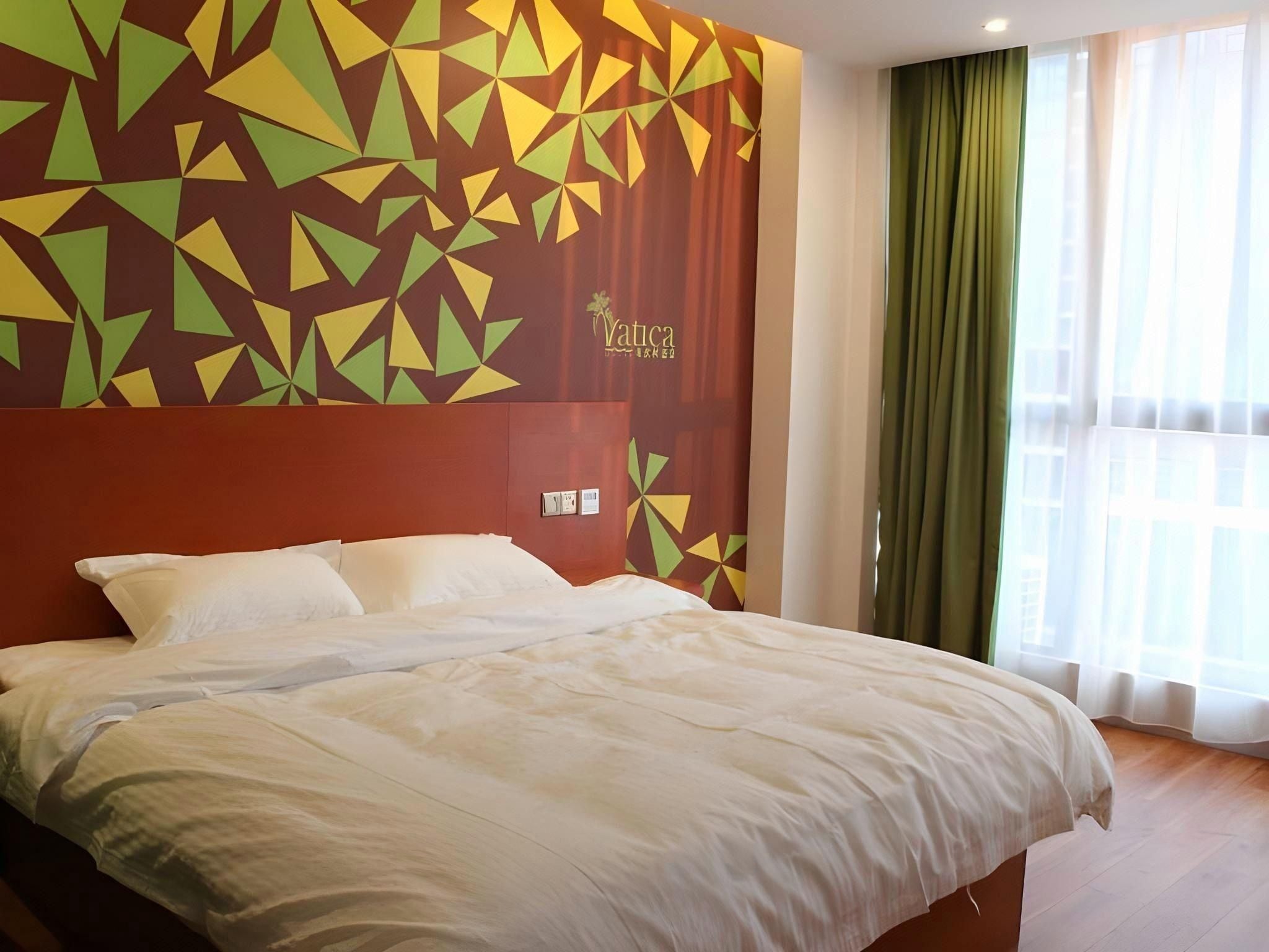 Quarto de hotel com uma cama grande, parede com padrão geométrico e janela com cortinas.