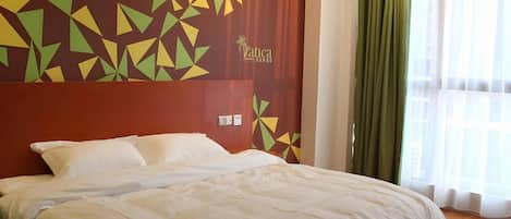 A hotel room with a large bed, a geometric patterned wall, and a window with curtains.