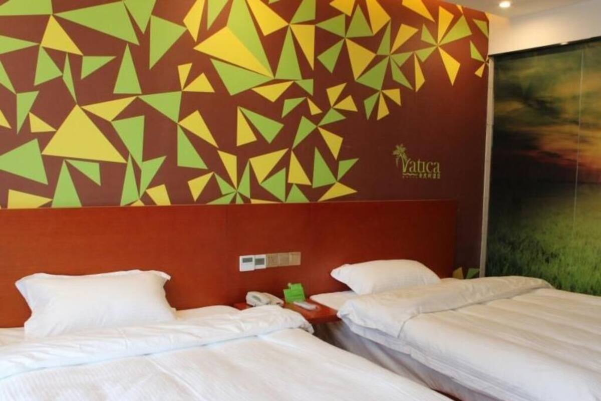 Quarto de hotel com duas camas, parede vermelha com padrões geométricos e vista parcial de uma paisagem verde.