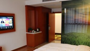 A hotel room with a bed, a television, a small kitchenette, and a door leading to another room. - Vatica Hotel Fuyang Linquan Tenghui International City Branch (Fuyang)