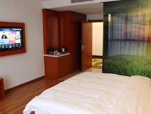 A hotel room with a bed, a television, a small kitchenette, and a door leading to another room. - Vatica Hotel Fuyang Linquan Tenghui International City Branch (Fuyang)