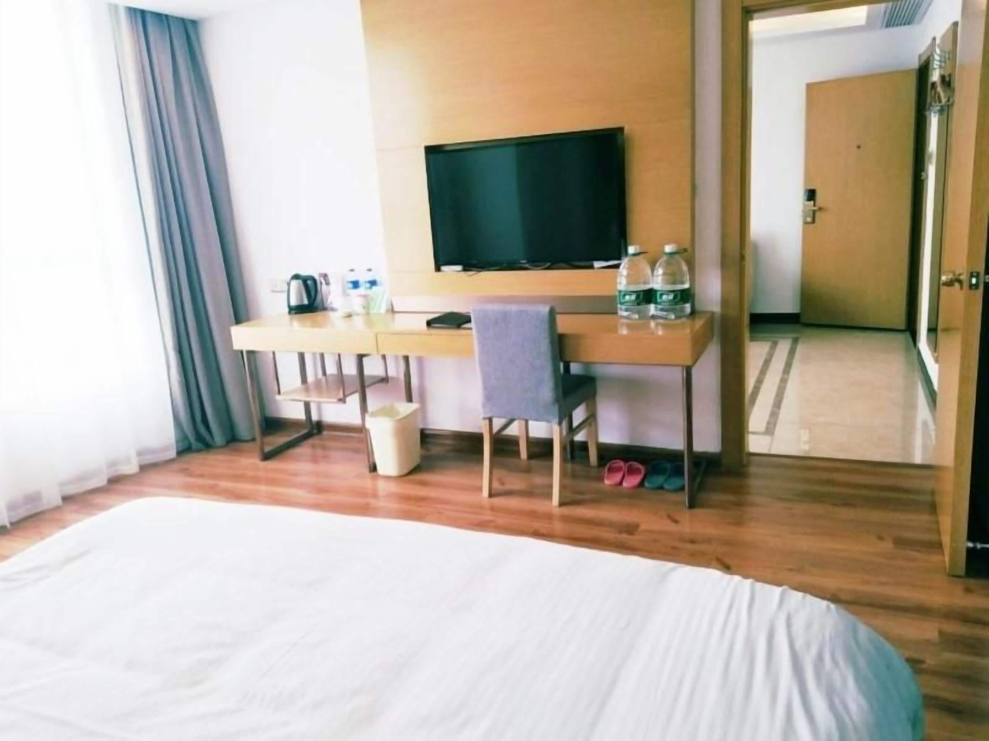 Una habitación de hotel con una cama, un escritorio con una silla, un televisor y una puerta.
